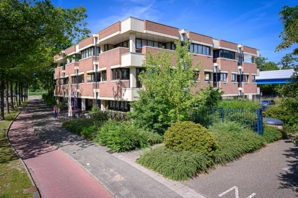Bakstenen kantoorgebouw De Linie met groenvoorziening en fietspad aan de voorzijde op een zonnige dag.
